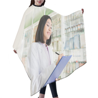 Personality  Cheerful Asian Pharmacist In White Coat Holding Pen Near Clipboard In Drugstore  Hair Cutting Cape
