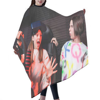 Personality  Amazed Girl On Car Simulator Gesturing Near Surprised Friend Hair Cutting Cape