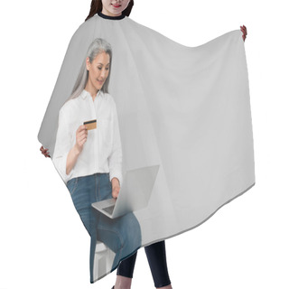 Personality  Smiling Asian Woman With Credit Card Sitting On Stool And Using Laptop Isolated On Grey Hair Cutting Cape