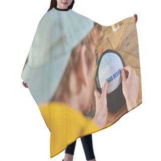 Personality  Blurred Young Designer Holding Printing Layer Near Snapback While Working Near Blurred Coffee To Go On Table In Print Studio, Hands-on Entrepreneurship Concept  Hair Cutting Cape