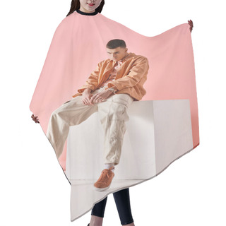 Personality  Stylish Man In Beige Shirt, Pants And Sneakers Sitting On White Cube On Pink Background Hair Cutting Cape