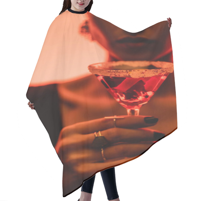 Personality  margarita cocktail with salt on glass in hand of woman on blurred orange background  hair cutting cape