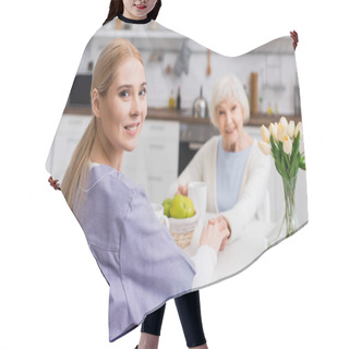 Personality  Young Nurse Smiling At Camera While Holding Hands With Senior Woman On Blurred Background Hair Cutting Cape