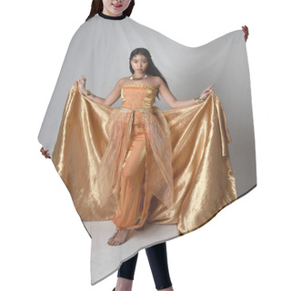 Personality  Full Length Portrait Of Pretty Young Asian Woman Wearing Golden Arabian Robes Like A Genie, Standing Pose Holding Flowing Fabric, Isolated On Studio Background. Hair Cutting Cape
