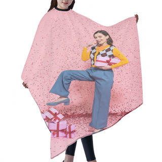 Personality  Joyful Woman In Blue Pants Holding Gift Box While Posing Near Pile Of Presents And Confetti On Pink Background Hair Cutting Cape