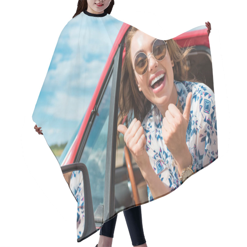 Personality  excited young woman in sunglasses sitting in car and showing thumbs up during trip hair cutting cape