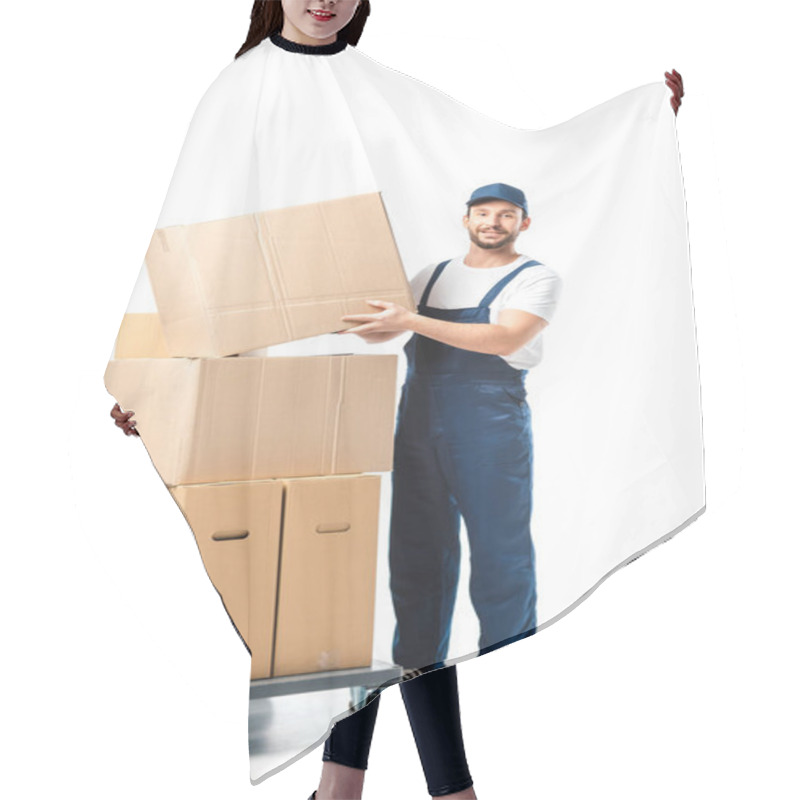 Personality  handsome mover in uniform transporting cardboard box near hand truck with packages isolated on white hair cutting cape
