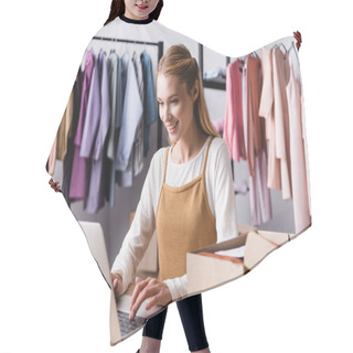 Personality  Smiling Showroom Proprietor Typing On Laptop Near Cardboard Boxes And Racks On Blurred Background Hair Cutting Cape