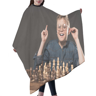 Personality  Happy Little Boy In Eyeglasses Doing Idea Gesture By Finger At Table With Chess Board Isolated On Grey Background  Hair Cutting Cape