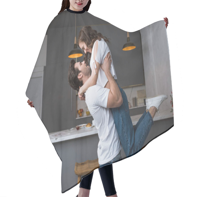 Personality  handsome man holding in arms attractive girlfriend in modern kitchen  hair cutting cape