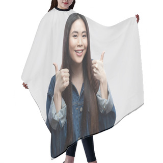 Personality  Satisfied Beautiful Brunette Asian Young Woman In Casual Blue Denim Jacket Showing Thumbs Up And Toothy Smiling While Looking At Camera On Light Grey Background. Hair Cutting Cape