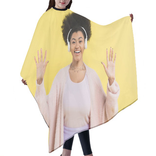 Personality  Optimistic African American Woman In Wireless Headphones And Cardigan Waving Hands And Looking At Camera Isolated On Yellow Hair Cutting Cape