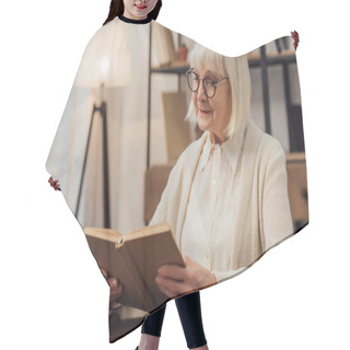 Personality  Thoughtful Senior Woman In Glasses Sitting At Table And Reading Book At Home Hair Cutting Cape