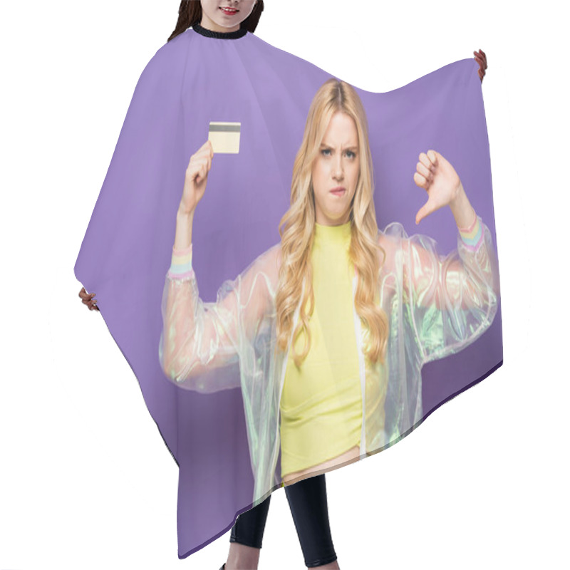 Personality  sad blonde young woman in colorful outfit showing credit card and thumb down on purple background hair cutting cape