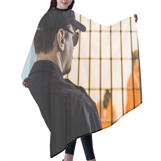 Personality  Rear View Of Prison Officer Standing Near Prison Cell With Criminals Hair Cutting Cape