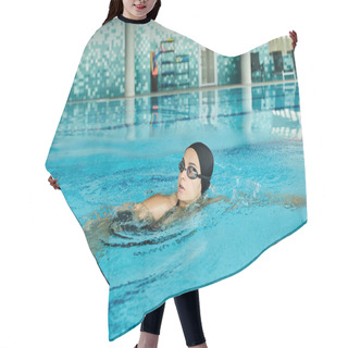 Personality  A Young Woman In A Swimsuit, Swim Cap, And Goggles Gracefully Swims In An Indoor Pool. Hair Cutting Cape