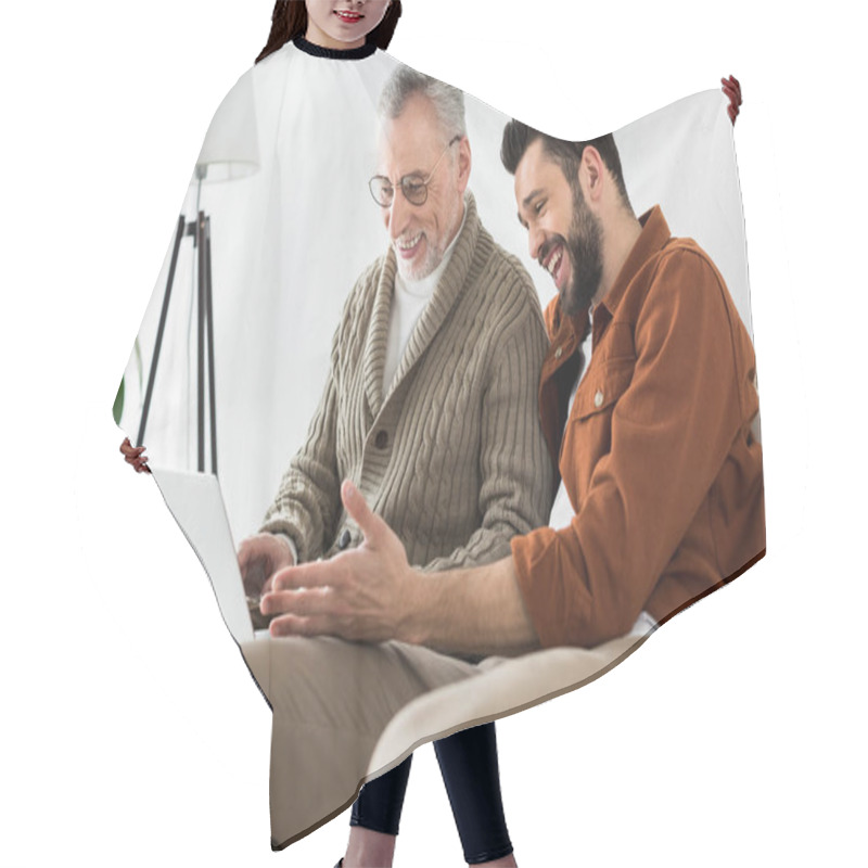 Personality  Cheerful Bearded Man Gesturing While Sitting With Senior Father And Looking At Laptop  Hair Cutting Cape