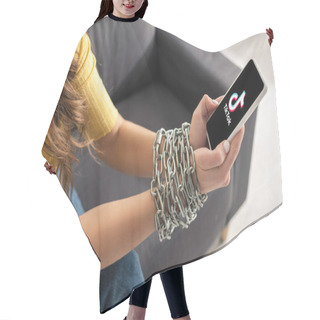 Personality  KYIV, UKRAINE - FEBRUARY 21, 2020: Cropped View Of Young Woman Holding Smartphone With TikTok App In Tied Hands With Metal Chain On Couch  Hair Cutting Cape