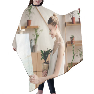 Personality  Side View Of Smiling Young Woman Holding Potted Plant And Painting Picture In Art Studio Hair Cutting Cape