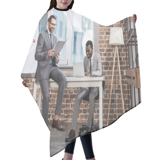 Personality  Smiling Businessman Sitting On Table And Reading Document While African American Partner Working On Laptop In Officeac Hair Cutting Cape