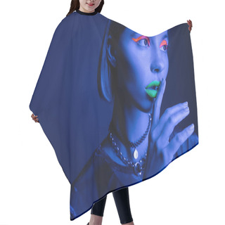 Personality  Portrait Of Woman In Neon Makeup Touching Green Lips While Showing Hush Sign On Dark Blue Background Hair Cutting Cape