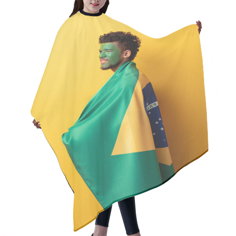 Personality  smiling african american football fan with painted face wrapped in brazilian flag on yellow hair cutting cape