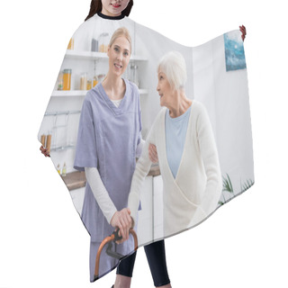 Personality  Young Nurse Smiling At Camera While Supporting Aged Woman Near Medical Walkers Hair Cutting Cape