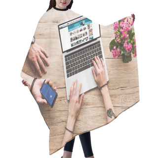 Personality  Cropped Shot Of Man With Smartphone With Facebook Logo In Hand And Woman At Tabletop With Laptop With Amazon Website And Kalanchoe Flower Hair Cutting Cape