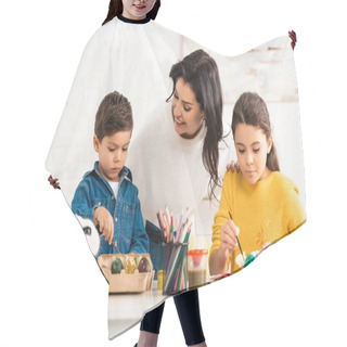 Personality  Happy Woman Looking At Adorable Children Painting Easter Eggs While Sitting At Table Near White Rabbit In Wicker Hair Cutting Cape