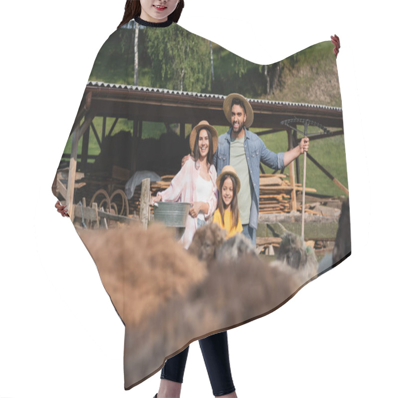 Personality  family in straw hats smiling near corral and livestock on blurred foreground hair cutting cape