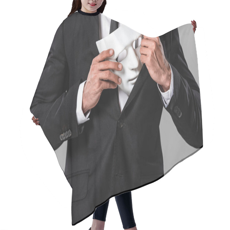 Personality  partial view of businessman in black suit holding white mask isolated on grey hair cutting cape