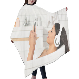 Personality  Side View Of Smiling Young Woman Listening Music In Headphones Looking At Cellphone In Bathroom Hair Cutting Cape