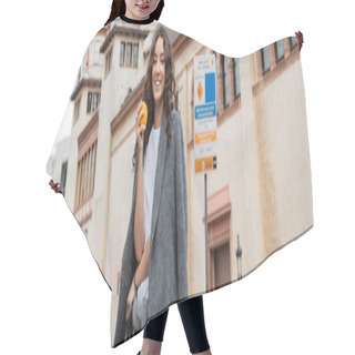 Personality  Young Curly Woman In Casual Grey Jacket Holding Ripe And Fresh Orange And Smiling At Camera With Historical Landmark At Background Outdoors In Barcelona, Spain, Banner, Ancient Building  Hair Cutting Cape