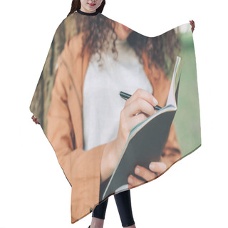 Personality  Cropped View Of Young Woman Writing On Notebook Near Tree In Park  Hair Cutting Cape