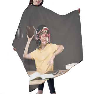 Personality  Schoolboy In American Football Helmet Throwing Ball And Sitting At Table With Books, Plant, Lamp, Colour Pencils, Apple, Clock And Textbook On Grey Background  Hair Cutting Cape