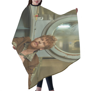 Personality  Stylish Redhead And Bearded Young Man Looking At Camera From Washing Machine In Coin Laundry Hair Cutting Cape