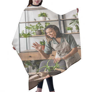 Personality  Smiling African American Florist In Apron Waving Hand Near Laptop During Video Call In Flower Shop Hair Cutting Cape