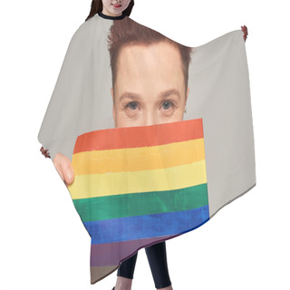 Personality  Joyful Redhead Queer Person Obscuring Face With Small LGBT Flag And Looking At Camera On Grey Hair Cutting Cape