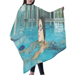 Personality  A Young Woman In A Swimsuit And Swim Cap Swimming In A Pool With Goggles On, Creating Ripples In The Water. Hair Cutting Cape