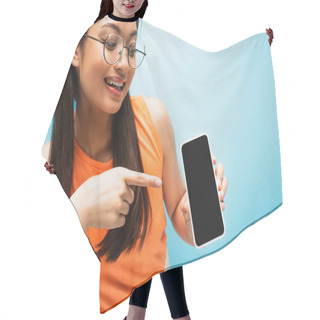 Personality  Cheerful Asian Girl In Glasses Pointing With Finger At Smartphone With Blank Screen On Blue Hair Cutting Cape