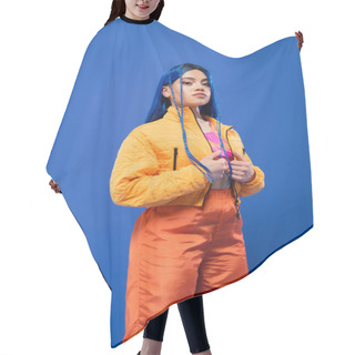 Personality  Dyed Hair, Fashion Forward, Tattooed Female Model With Blue Hair Posing In Puffer Jacket And Orange Pants On Blue Background, Vibrant Color, Urban Fashion, Individualism, Young Woman  Hair Cutting Cape