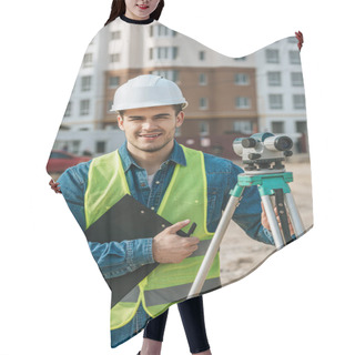 Personality  Surveyor Holding Clipboard And Digital Level And Smiling At Camera On Construction Site Hair Cutting Cape