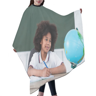 Personality  Smiling African American Pupil Writing On Notebook Near Blurred Globe On Desk  Hair Cutting Cape
