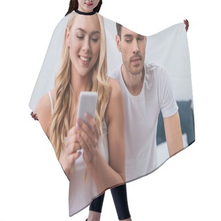 Personality  Jealous Man Looking At Beautiful Smiling Wife Using Smartphone In Bedroom, Mistrust Concept  Hair Cutting Cape