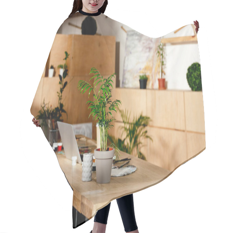 Personality  interior of artist studio with painting supplies, laptop and potted plants on wooden table  hair cutting cape