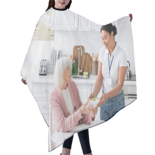Personality  Happy Multiracial Social Worker Holding Bowl With Salad For Senior Woman With Grey Hair  Hair Cutting Cape