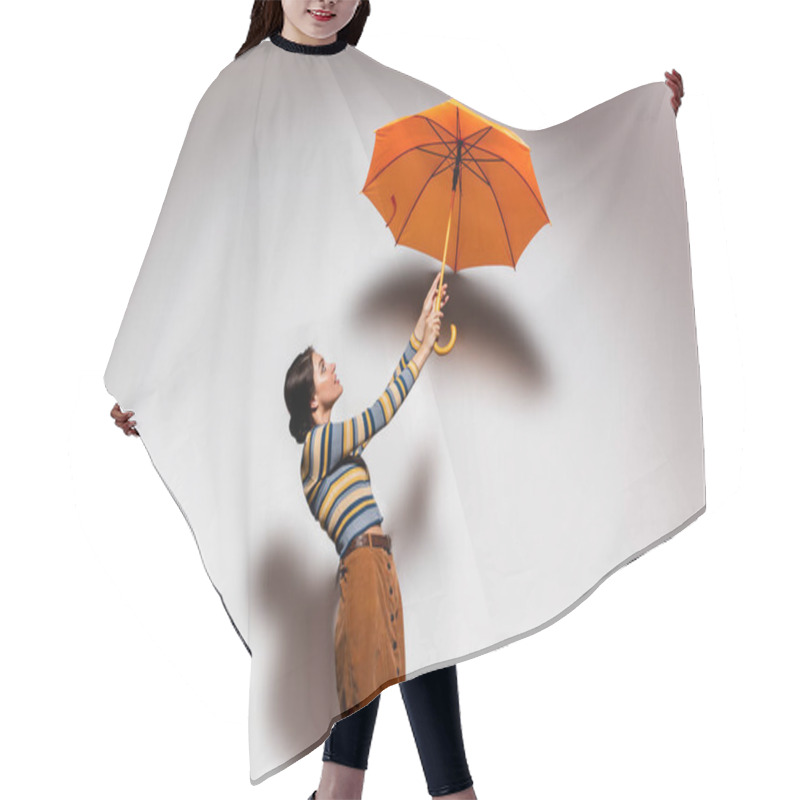 Personality  Side View Of Brunette Young Woman In Striped Turtleneck And Skirt Posing With Orange Umbrella On Grey Hair Cutting Cape