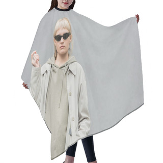 Personality  Stylish And Young Woman With Bangs And Blonde Hair Standing In Trendy Sunglasses And Comfortable Clothes While Looking At Camera And Posing With Hand In Pocket Isolated On Grey Background In Studio  Hair Cutting Cape