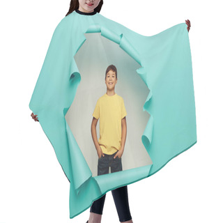 Personality  Smiling Multicultural Boy Holding Hands In Pockets Of Pants And Looking At Camera While Celebrating Child Protection Day Behind Hole In Blue Paper Background Hair Cutting Cape