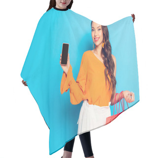 Personality  Happy Trendy Girl Holding Shopping Bags And Showing Smartphone With Blank Screen On Blue Background Hair Cutting Cape